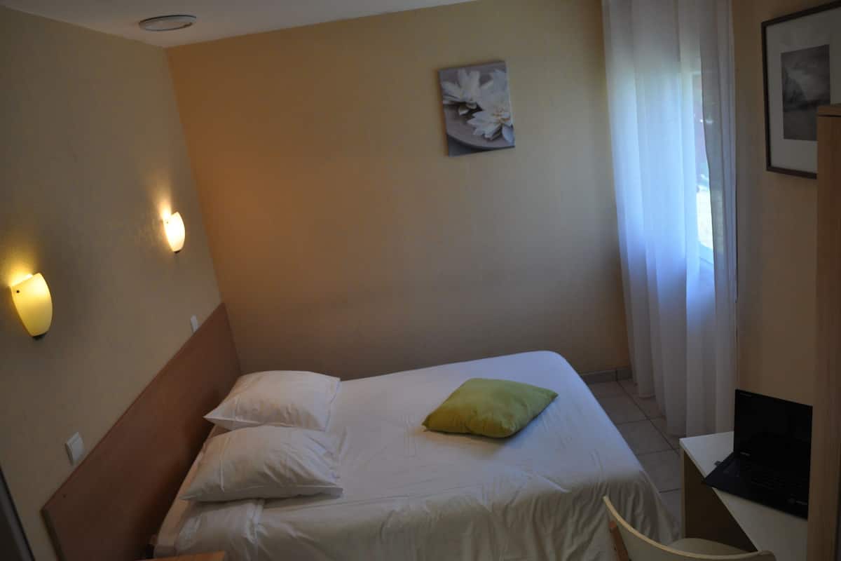 A hotel room with a bed, pillows, a laptop on a desk, and a painting on the wall.