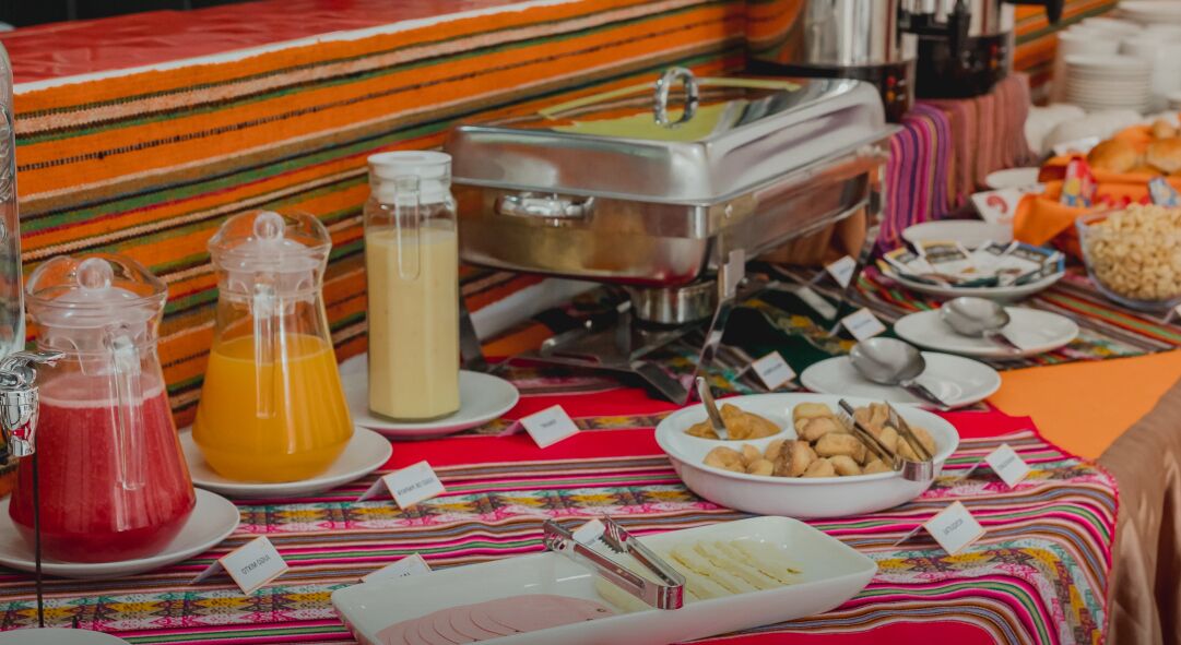 Una mesa de buffet con diversos alimentos y bebidas, incluyendo una jarra de jugo de naranja, una jarra de leche y un bol de galletas.