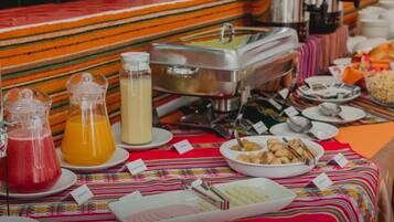 Una mesa de buffet con diversos alimentos y bebidas, incluyendo una jarra de jugo de naranja, una jarra de leche y un bol de galletas.