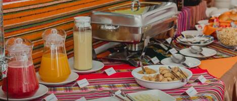 A buffet table with various food items and beverages, including a glass pitcher of orange juice, a glass pitcher of milk, and a bowl of cookies.