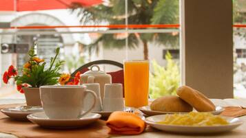 Una mesa de desayuno con un juego de café, jugo de naranja, pan y un plato de huevos revueltos.