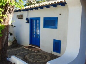 A white building with blue doors and windows, a tiled roof, and a stone-paved courtyard with potted plants. - Casa Amor do Mar (Búzios)