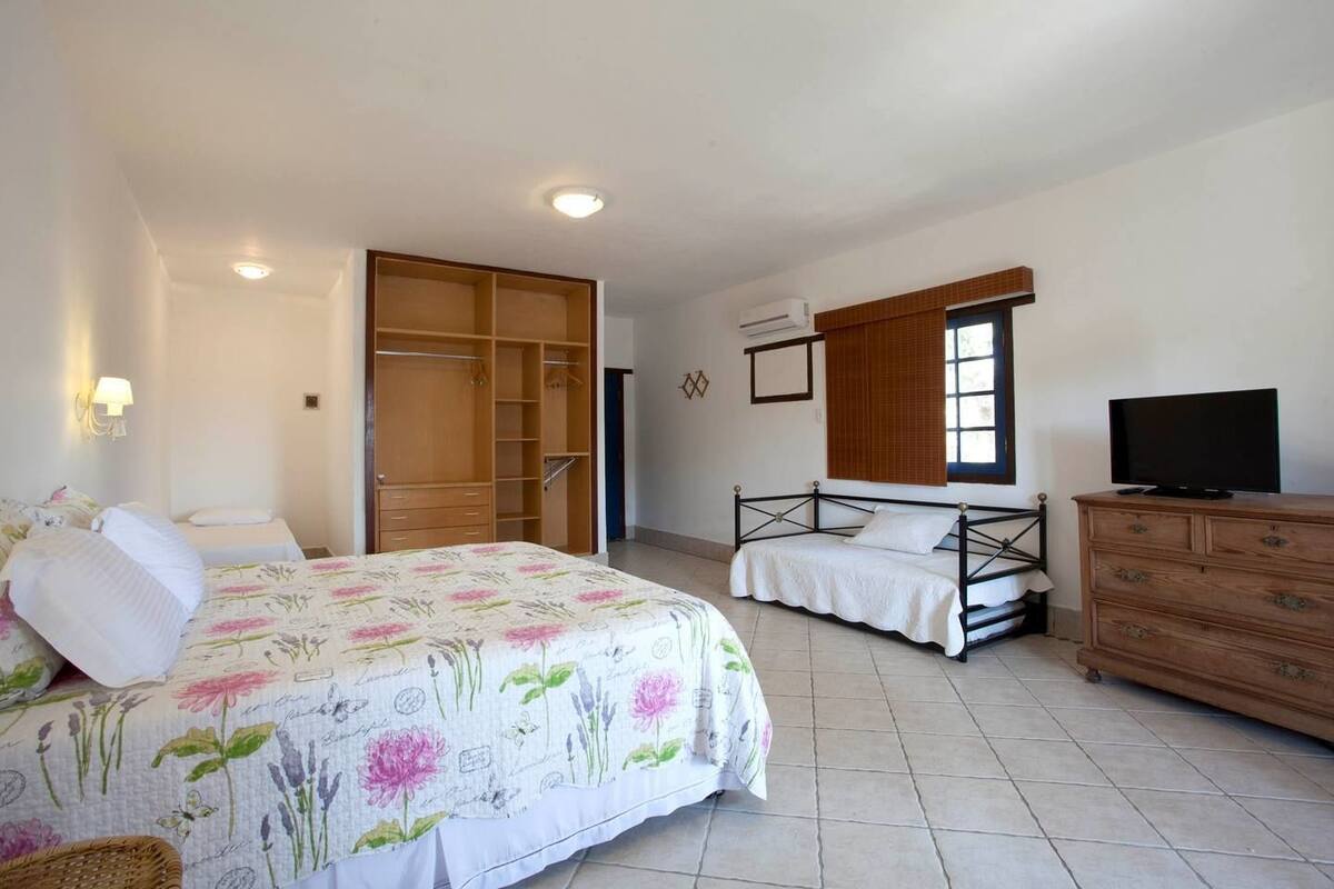 Un dormitorio con un armario amplio, una cama con ropa de cama floral, un televisor y una ventana con persianas.
