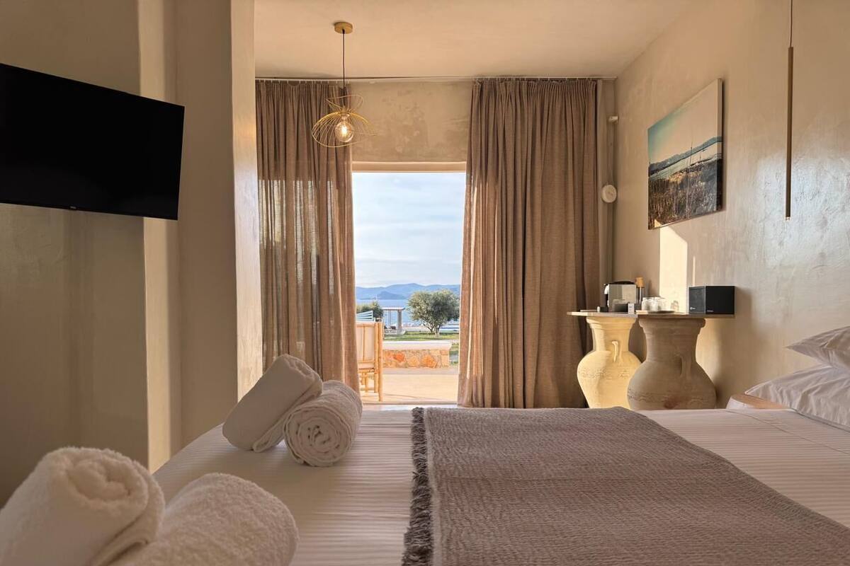 Habitación de hotel con cama, toallas, televisión, una mesa con lámpara y vistas al exterior.