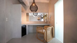 Un intérieur moderne avec un sol en béton, un grand miroir, des chaises en osier et un luminaire suspendu.