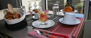 A breakfast setting with croissants, fruit, and a cup on a table with striped placemats. - Hotel Almadies (Saint-Jean-de-Luz)