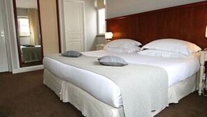 Ein Hotelzimmer mit einem großen Bett, zwei Nachttischen, einem Sessel und einem Holz-Kopfteil.