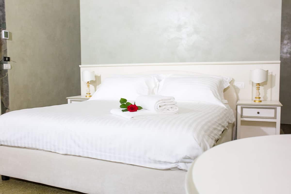 Un lit bien fait, avec du linge de lit blanc, une rose rouge et deux lampes de chevet.