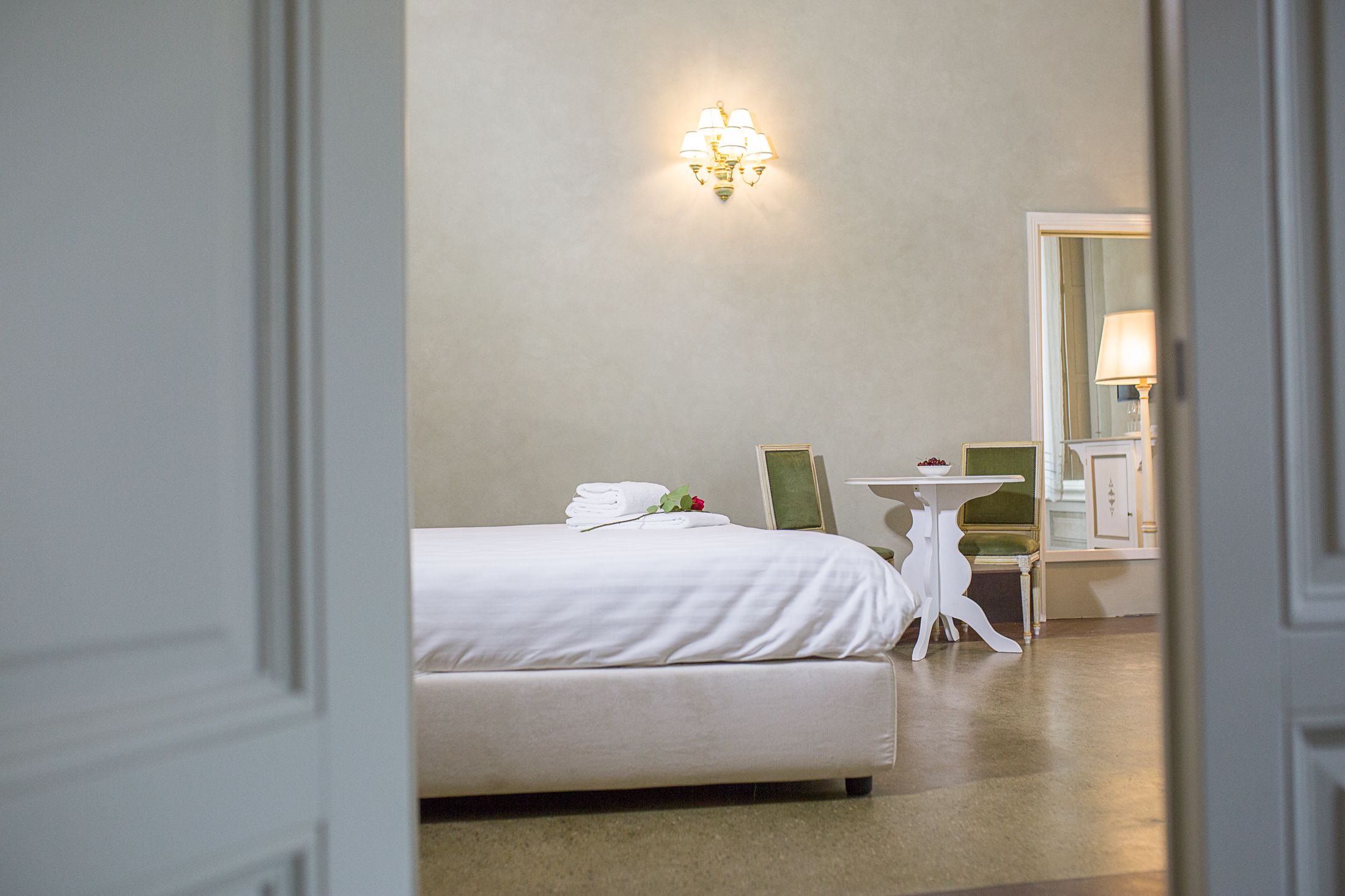 A hotel room with a neatly made bed, a small table with a chair, and a wall-mounted light fixture.