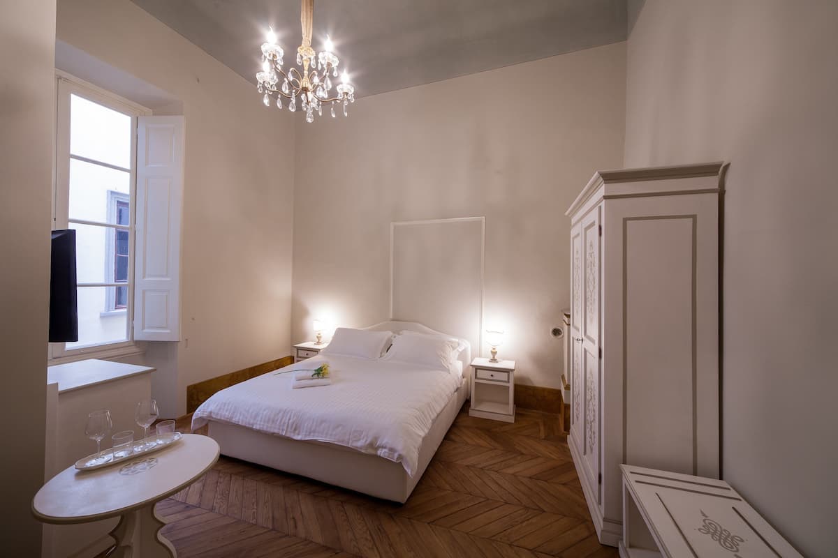 Une chambre à coucher avec un lit, des tables de chevet, un lustre, une armoire et une fenêtre.