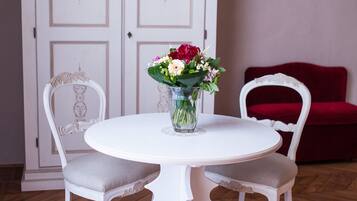 Un comedor con una mesa y sillas blancas, un jarrón con flores y un sofá rojo al fondo.