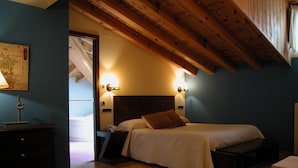 Een slaapkamer met een houten plafond, een bed met wit beddengoed, een nachtkastje en wandlampen.