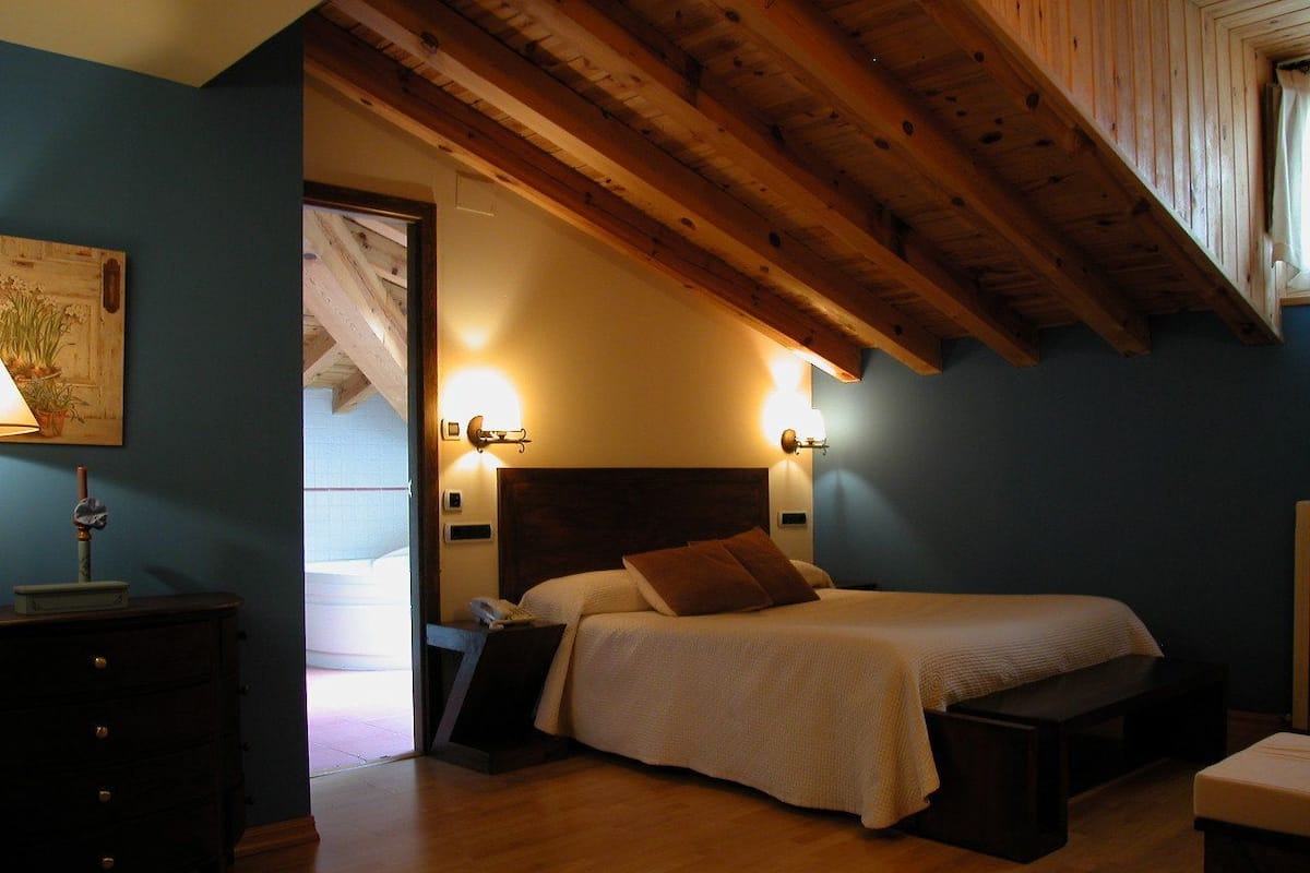Ein Schlafzimmer mit Holzboden, einem Bett mit weißer Bettwäsche, einem Nachttisch und Wandleuchten.