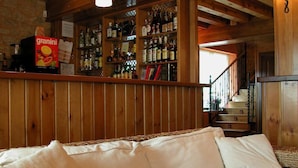 Een gezellige kamer met een rieten bank, houten balken in het plafond en een bar met verschillende flessen en een Granini sapje.