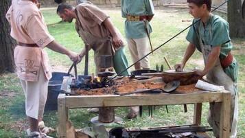 Un grup de persones participant en una activitat a l'aire lliure, possiblement una recreació històrica, amb una taula al centre que conté diverses eines i un foc.