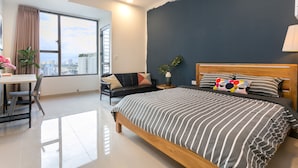 Un dormitorio moderno con una cama grande, un escritorio y vistas de la ciudad a través de un ventanal amplio.