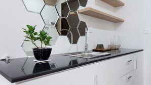 Una cocina moderna con encimera negra, armarios blancos, un salpicadero de espejo hexagonal y una planta en maceta.
