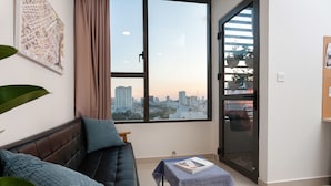 Un salón moderno con un sofá de cuero negro, una mesita con mantel a cuadros y un ventanal con vistas a la ciudad.
