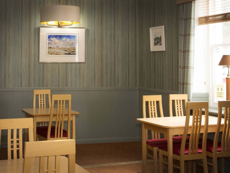 Comedor con mesas y sillas de madera, una lámpara de pared y cuadros enmarcados.