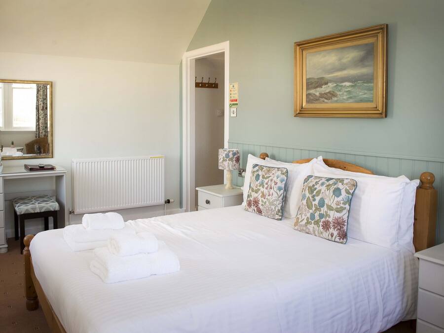 A neatly arranged bedroom with a large bed, a dresser, a mirror, and a painting on the wall.