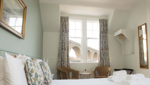 A hotel room with a bed, two chairs, a small table, a window with curtains, and a mirror on the wall. - The Royal Oak Hotel (Buckie)