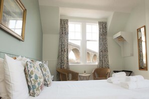 A hotel room with a bed, two chairs, a small table, a window with curtains, and a mirror on the wall. - The Royal Oak Hotel (Buckie)