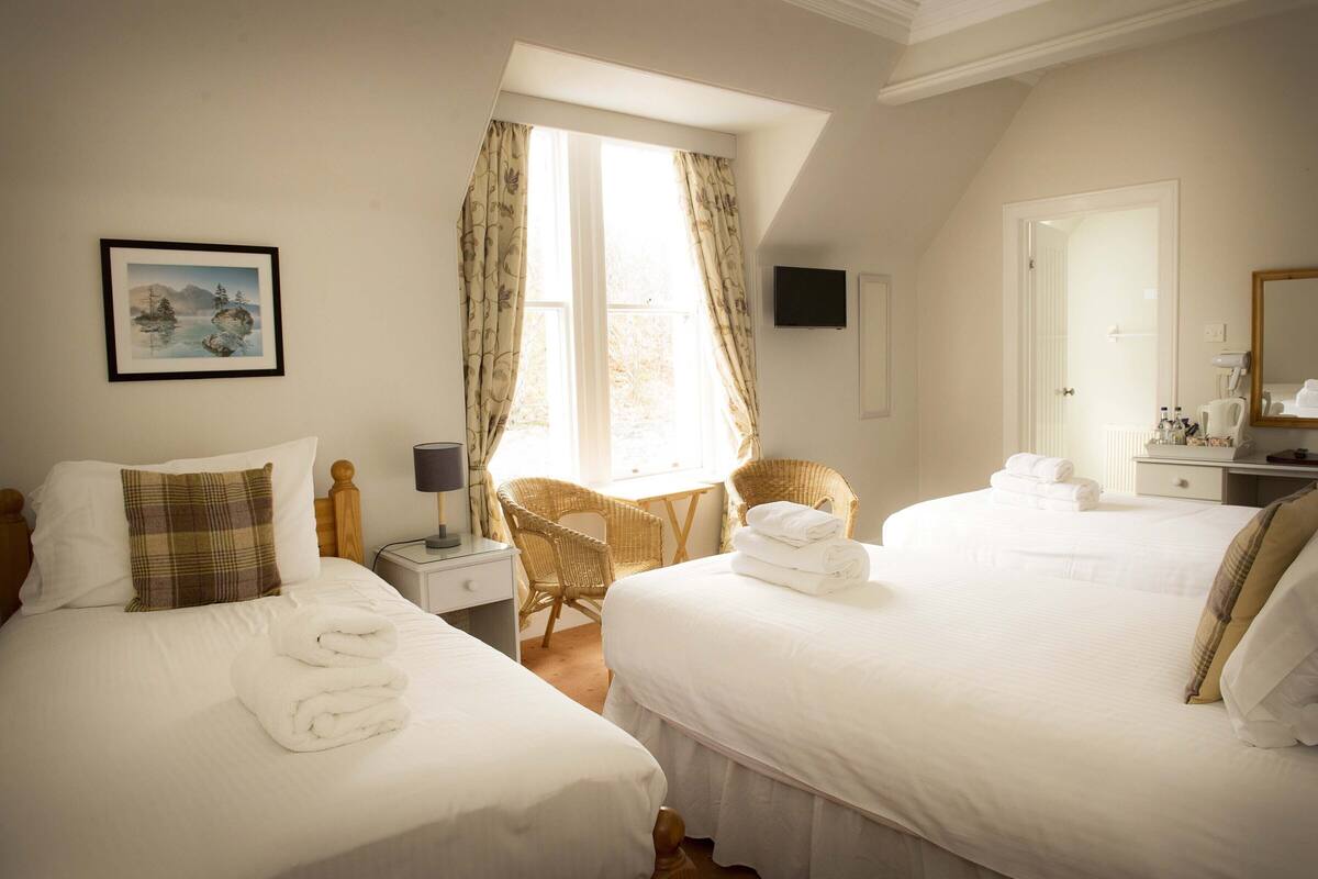 Habitación de hotel con dos camas, una silla, un escritorio y una ventana con cortinas.