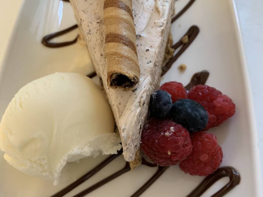 A dessert plate with a rolled wafer, ice cream, raspberries, and a mint leaf.