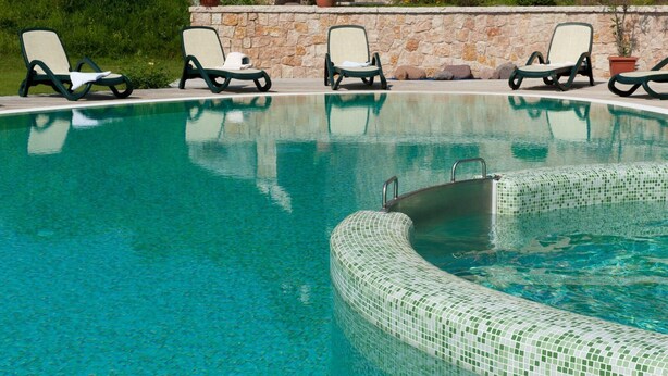 A swimming pool with a tiled edge, surrounded by lounge chairs and a stone wall. - La Quiete Resort (Romeno)