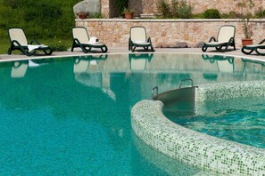 A swimming pool with a tiled edge, surrounded by lounge chairs and a stone wall. - La Quiete Resort (Romeno)