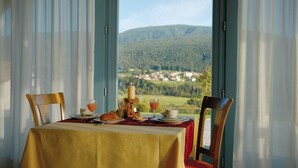 A dining table set with a tablecloth, chairs, and a view of a mountainous landscape through large windows. - La Quiete Resort (Romeno)