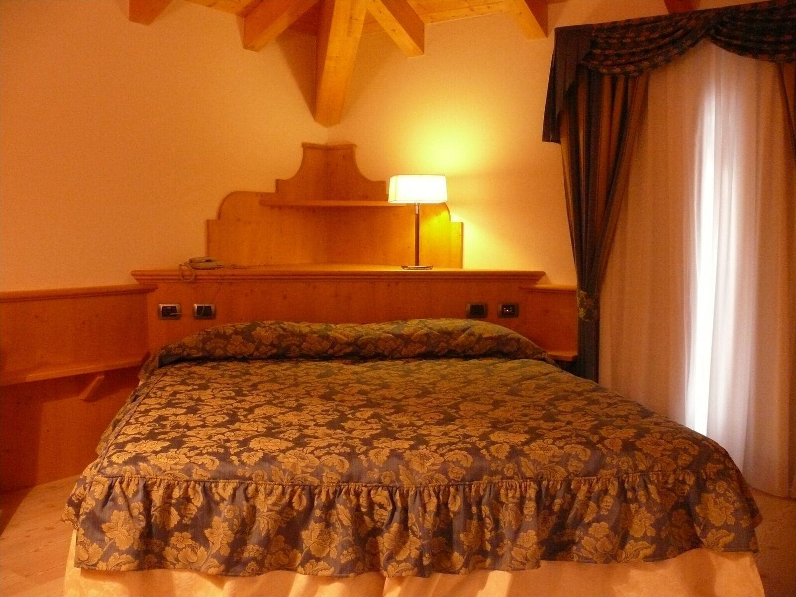 A hotel room with a bed, a nightstand, a lamp, and a window with curtains.