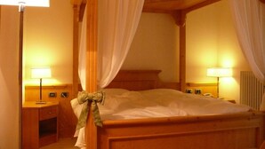 A four-poster bed with white drapes and a green bow, a bedside table with a lamp, and a wall with the text "LA QUETE". - La Quiete Resort (Romeno)