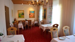 Un comedor con mesas dispuestas para cuatro, sillas de madera y una alfombra roja.