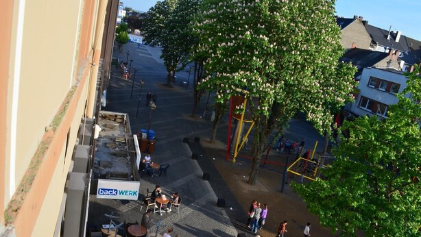 Un patio con mobiliario exterior, árboles y un parque infantil.
