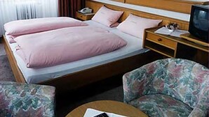 Una habitación de hotel con una cama doble, dos mesitas de noche, un televisor y un sillón tapizado con motivos florales.