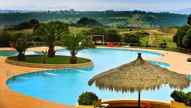 Una piscina con sombrilla de paja, palmeras y vistas a las colinas.