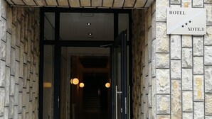 Een hotelentree met een gevel van natuursteen, een bord met de naam van het hotel en een glazen deur naar binnen.