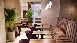 Een modern restaurantinterieur met marmeren vloeren, houten tafels, paars fluweel beklede stoelen en een lange, bekleedde bank.