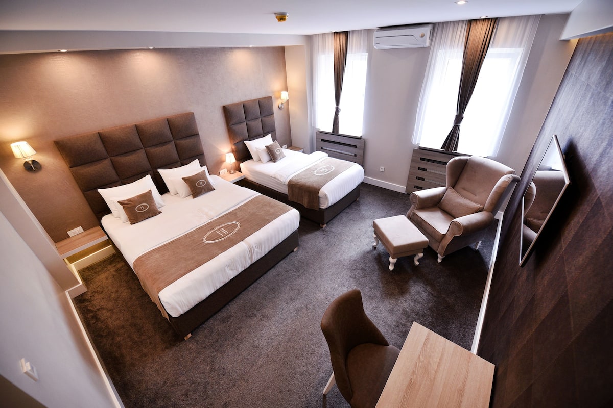 A hotel room with two beds, a sofa, a TV, and a desk.