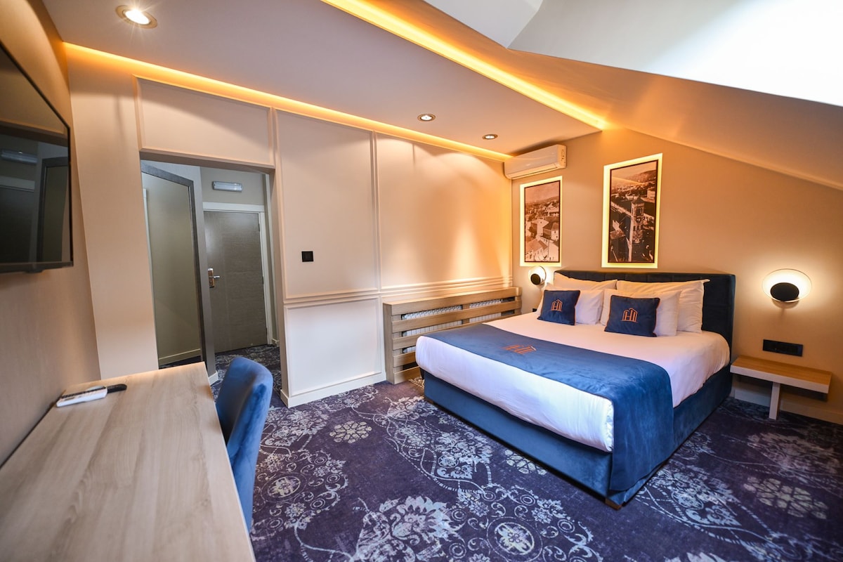 A hotel room with a bed, bedside tables, a desk, a chair, a mirror, and a door.