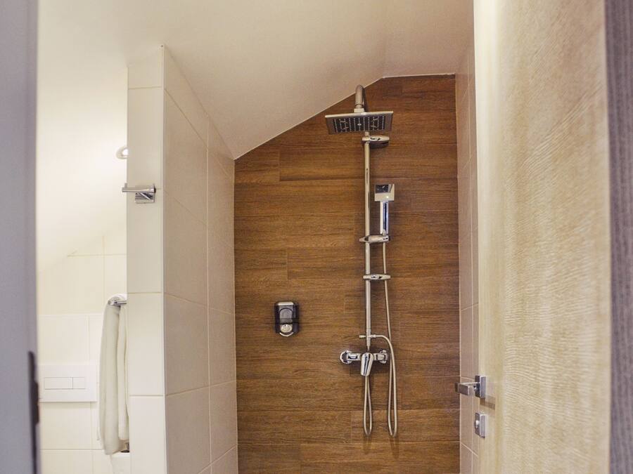 A modern shower with a wooden wall, a white toilet, and a towel on the floor.