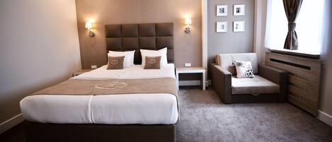 A modern hotel room with a large bed, a sofa, a nightstand, and a window with curtains.