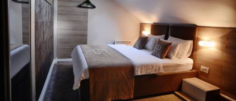 A bedroom with a sloped ceiling, a bed with a wooden headboard, a bedside table, and a wall-mounted heater.