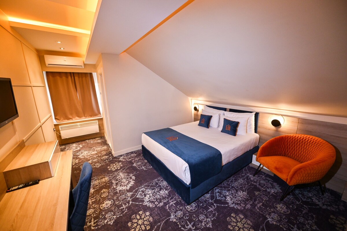 A hotel room with a bed, a chair, a desk, and a television.
