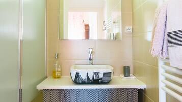 Un baño con cabina de ducha de vidrio, un lavabo con espejo y un perchero con toallas.
