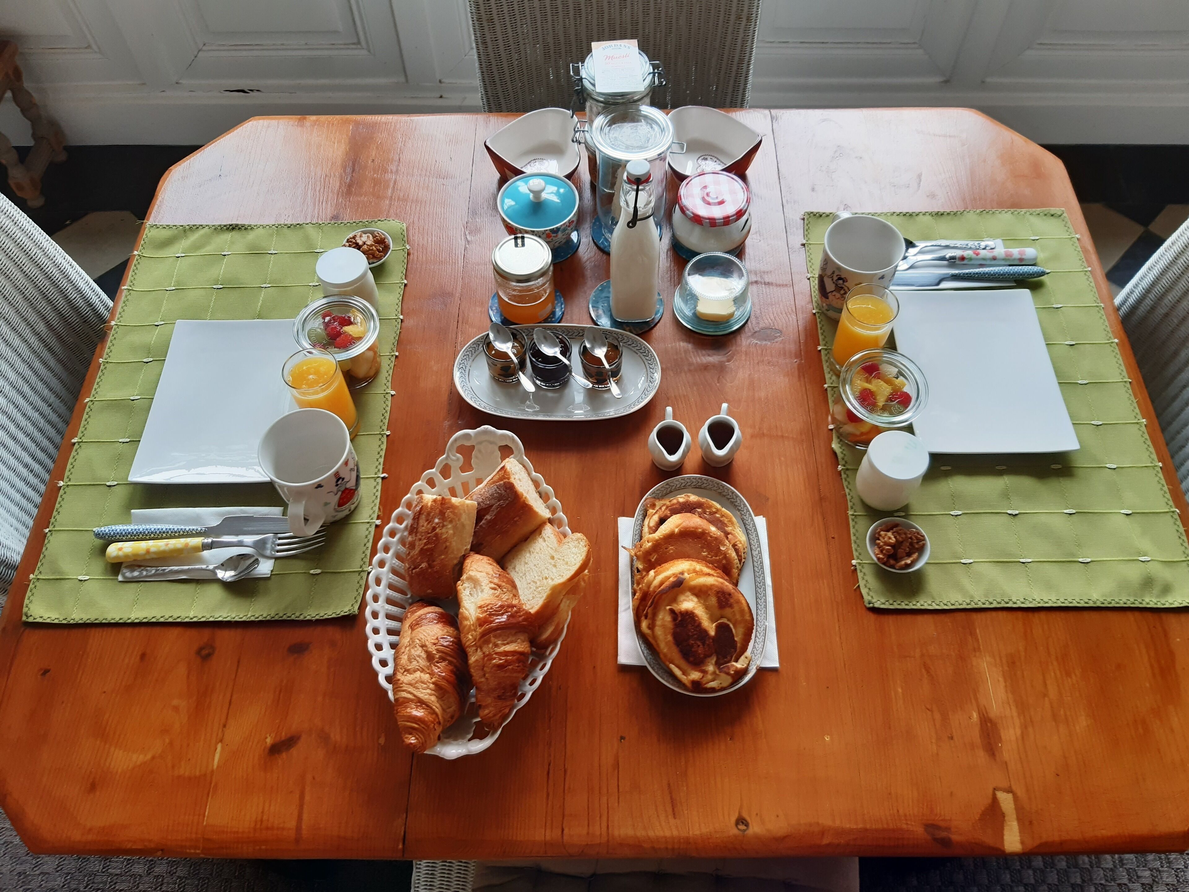 Una mesa de madera dispuesta para el desayuno, con cruasanes, pan, fruta y salsas.