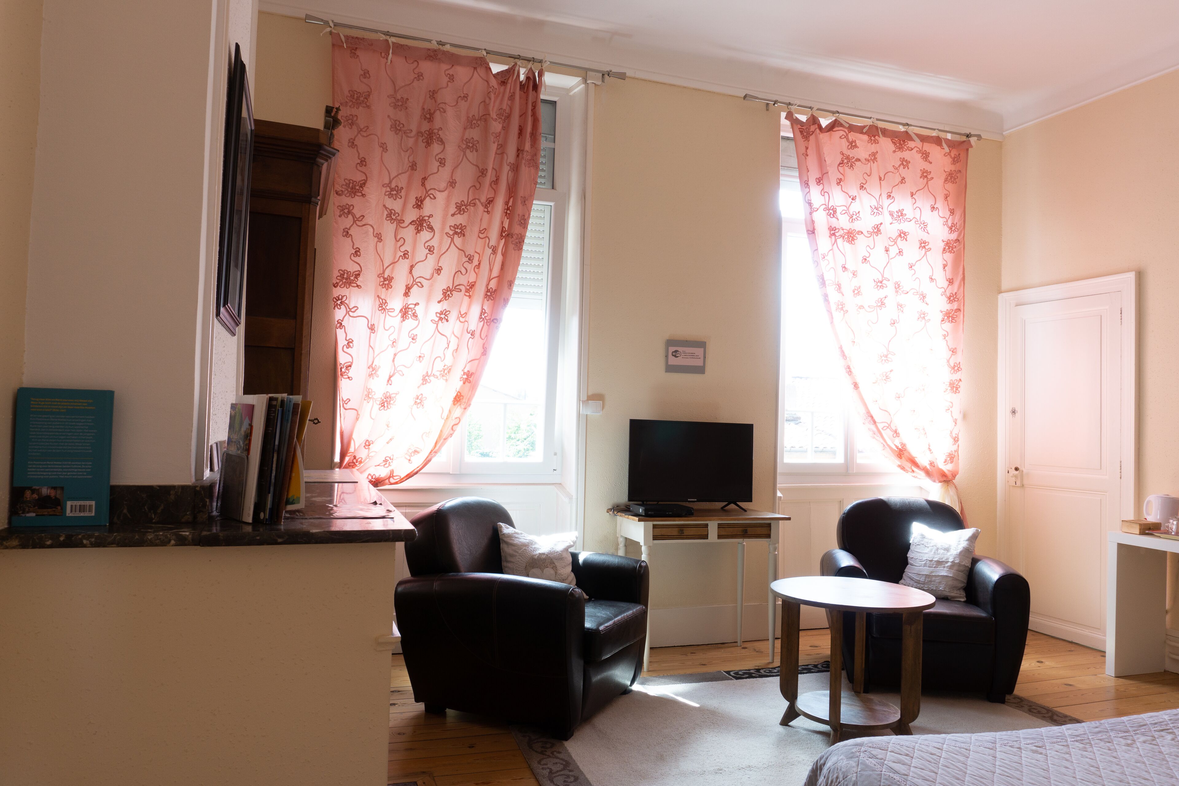Una habitación con dos sillones de cuero negro, una mesita redonda pequeña, un televisor sobre un soporte blanco y una estantería con libros.
