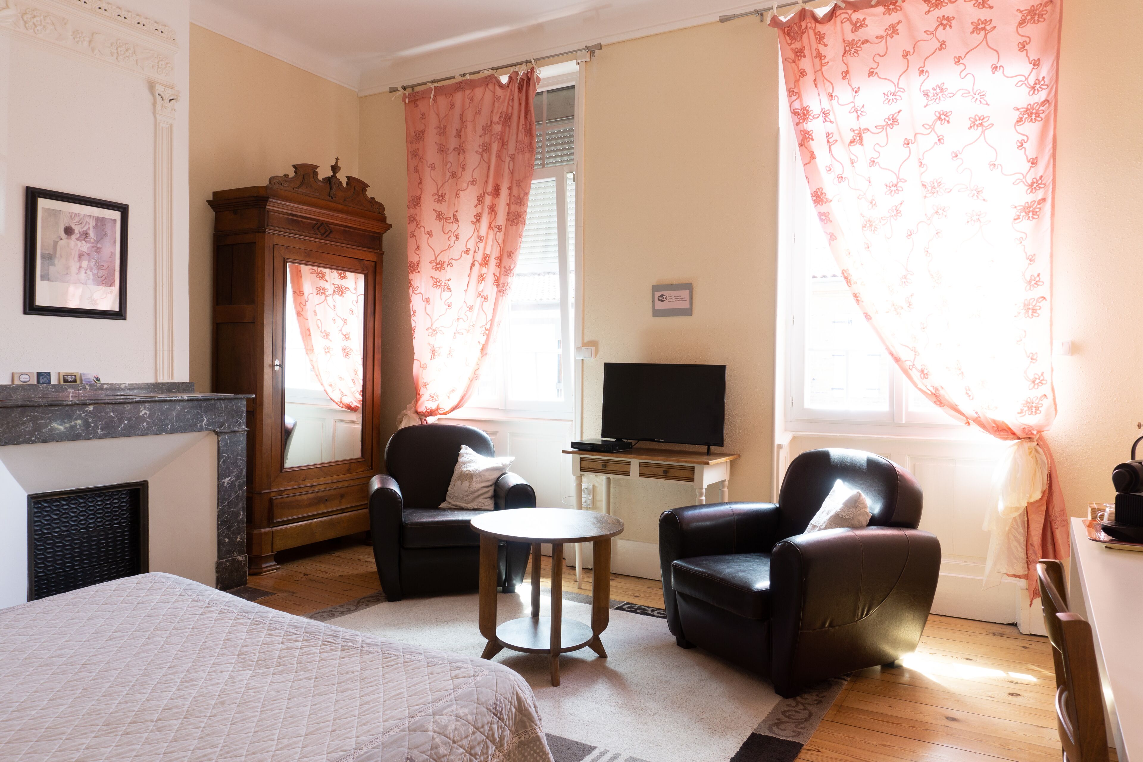 Habitación de hotel con cama, dos sillones, una mesita, televisión, chimenea y cortinas.