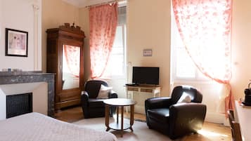 Habitación de hotel con cama, dos sillones, una mesita, televisión, chimenea y cortinas.